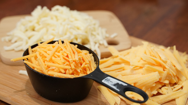 Measuring cup of grated cheddar on wood boards with other grated cheeses