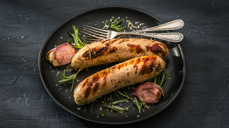 Two grilled sausages on a plate with garnishes and two forks