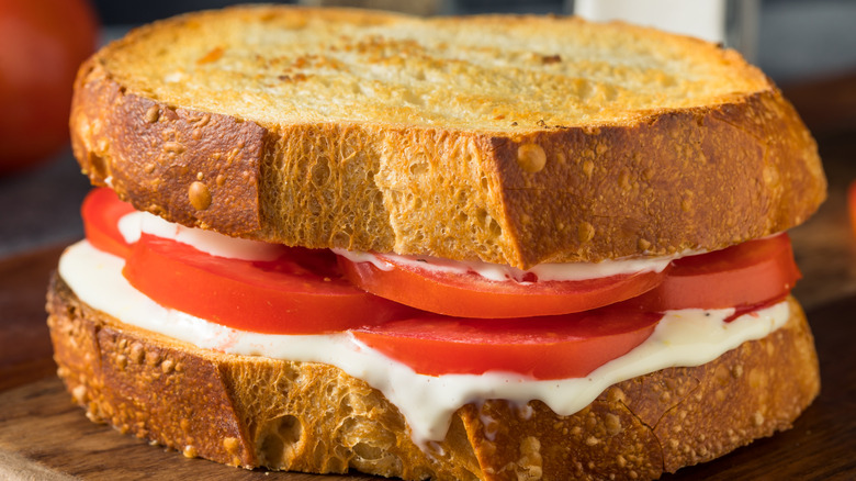Tomato sandwich with mayo on wooden cutting board