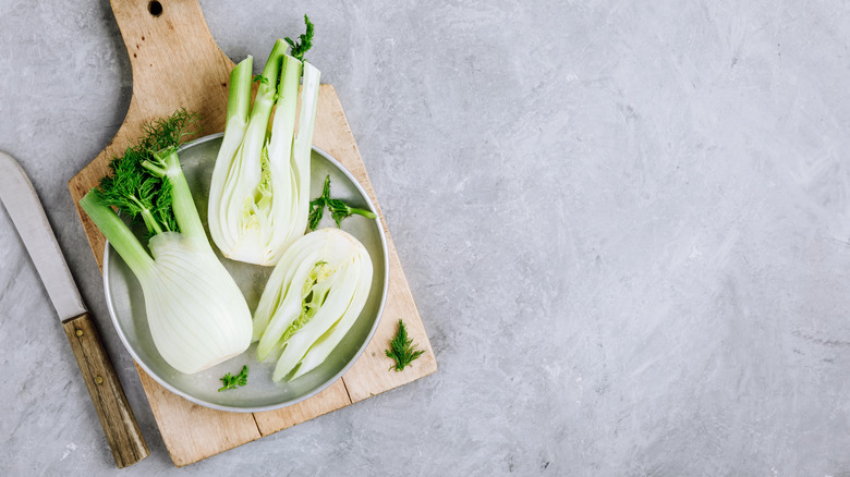 halved fennel bulbs on wooden board next to knife