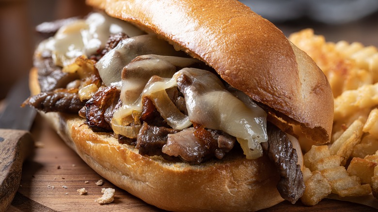 Cheesesteak and fries on wooden board