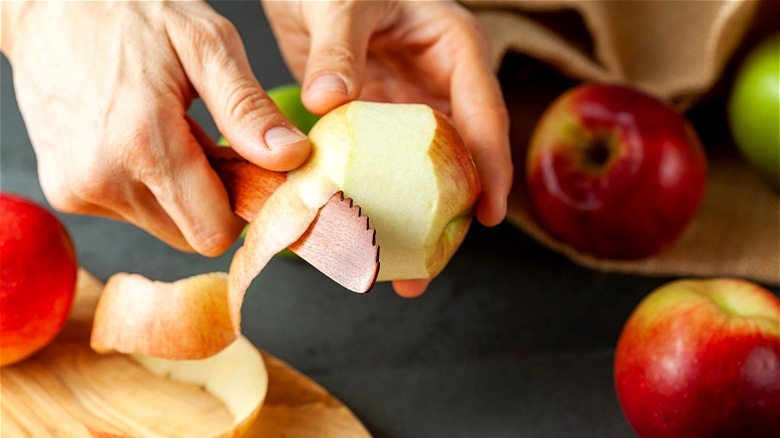 Hands peeling apple with wooden knife