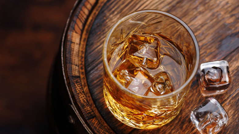 crystal glass of whiskey on the rocks sitting atop an aging barrel