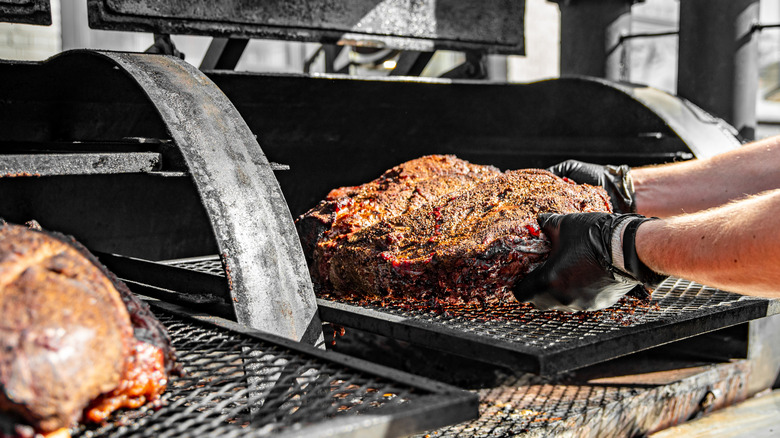 Person placing meat inside barrel smoker.