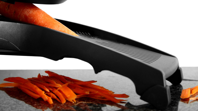 Hand using mandoline slicer for carrot