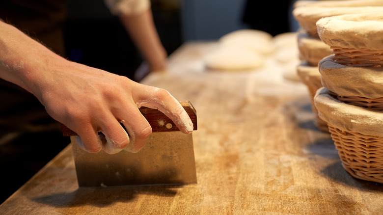 A hand scraping a large wooden baking bench with a bench scraper