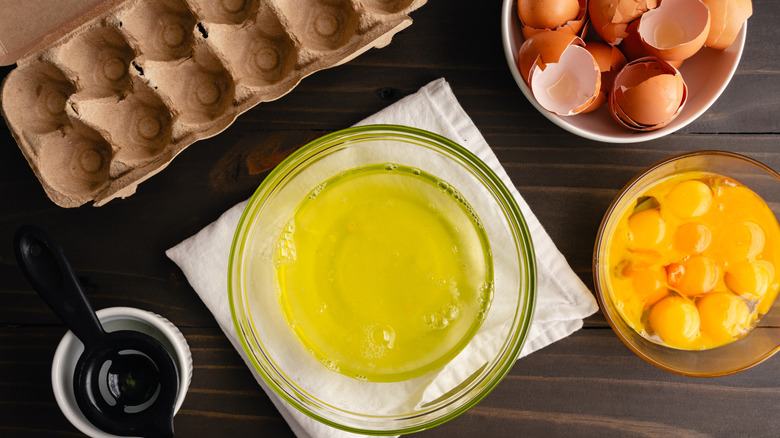 Egg yolk and egg white in separate bowls with empty egg carton and bowl of shells