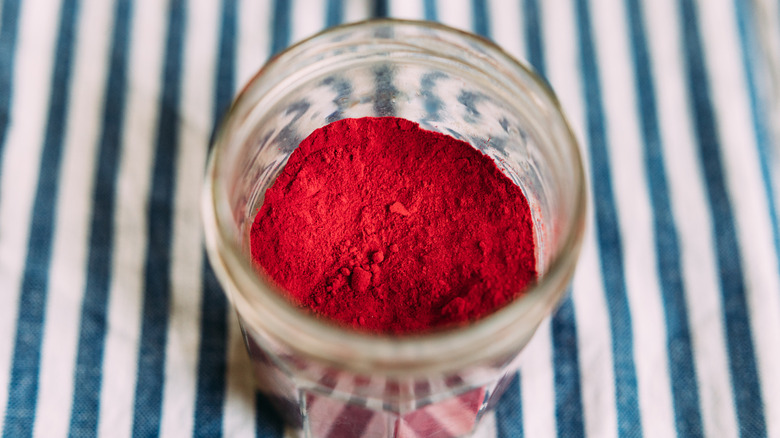 A small, clear jar of fine red powder, on a blue and white striped tablecloth