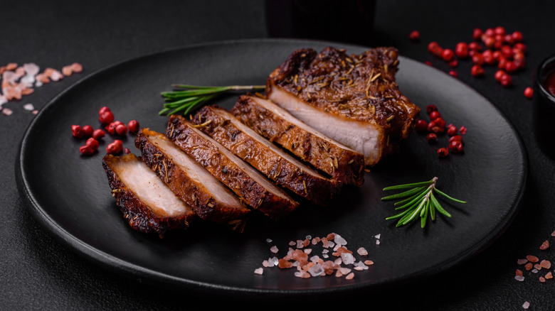 Pork steak on black plate with various garnished and dark background
