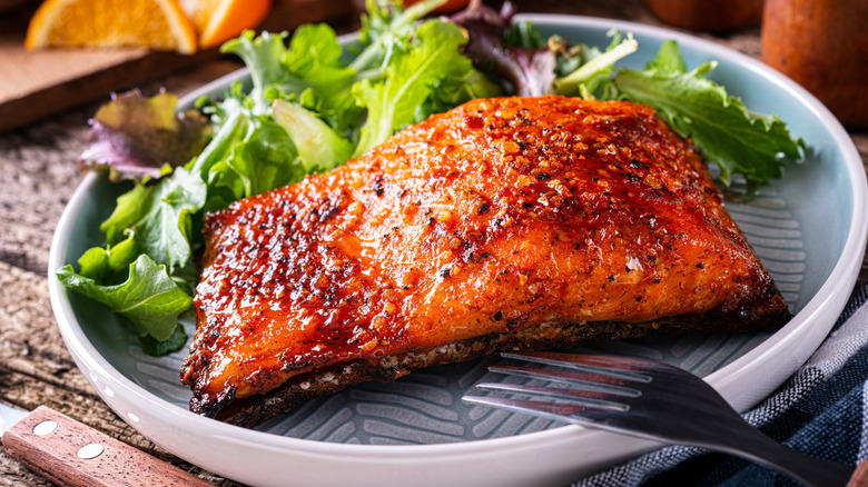 Glazed salmon on a plate with mixed greens on a table.