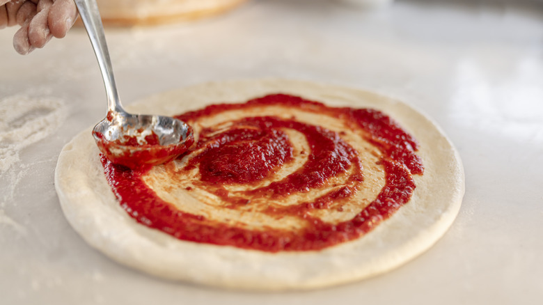 Ladle spreading sauce on pizza dough that doesn't have any cheese yet