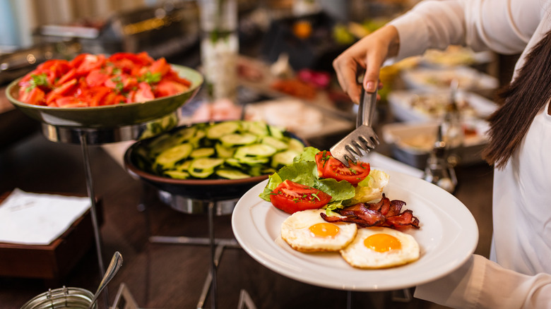 person grabbing tomato for breakfast buffet plate