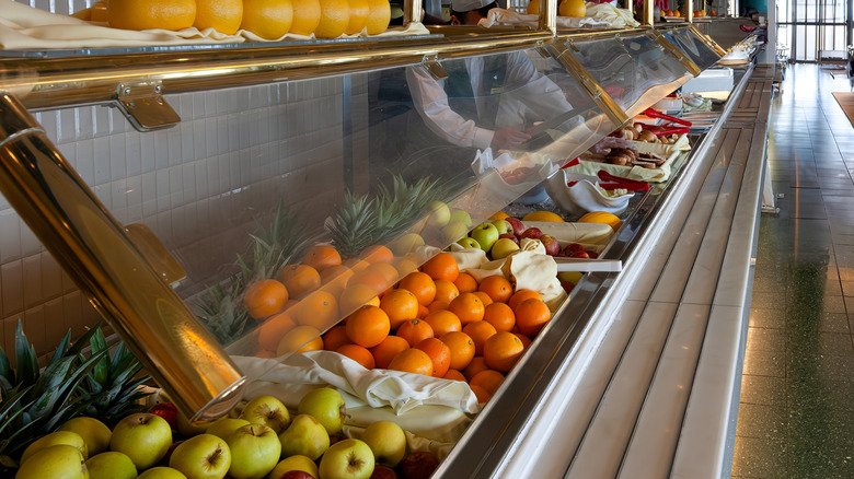 Cruise ship buffet featuring fruit and other items covered by sneeze guard