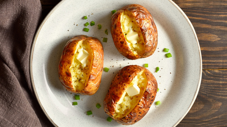 Oven-baked potatoes with butter on white plate by napkin