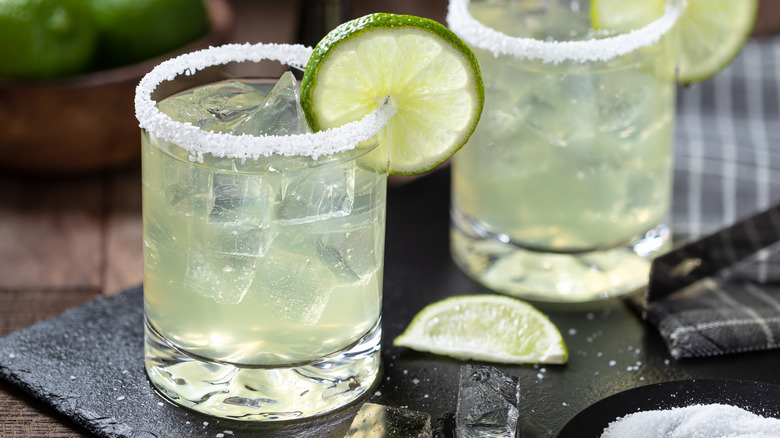 Two margaritas with salted rims and lime wedges