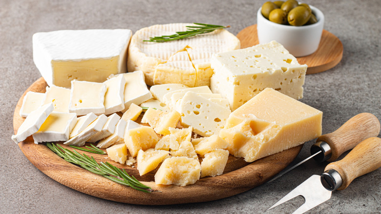 An assortment of white cheeses on a brown wooden tray, including brie, Camembert, and Parmesan