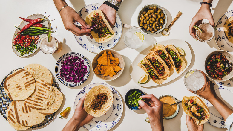 People assembling tacos with a variety of toppings laid out