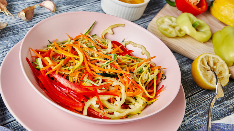 A bowl of bright, thinly sliced veggies in a pink bowl
