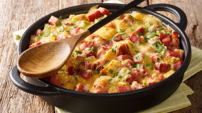 Breakfast strata in a baking dish with wooden spoon