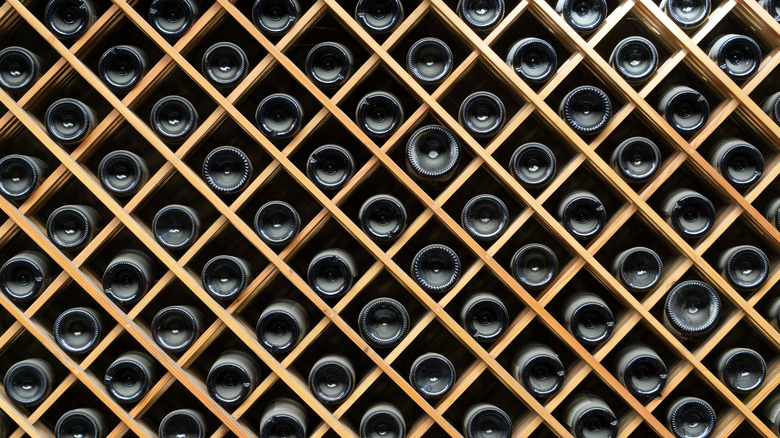 dozens of wine bottles stored in a wooden shelf showing the bottom dent