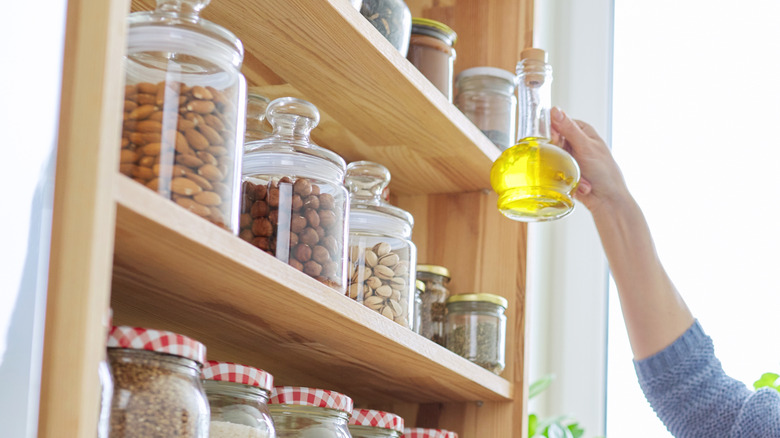 Woman picks up oil off pantry shelf lined with glass containers