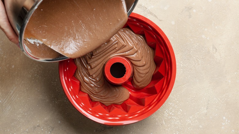 chocolate cake batter being poured into a red bundt pan