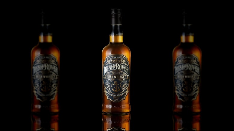 A clear glass bottle of Irish Rover whiskey with a black and gold label and black screw top.