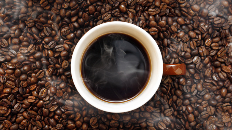 A cup of hot coffee surrounded by coffee beans 