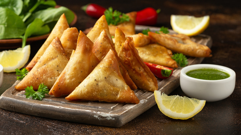 Samosas are served with mint chutney, coriander, and lemon.