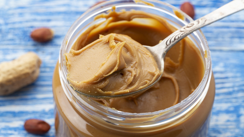 Spoonful of peanut butter being scooped out of jar with peanuts in background