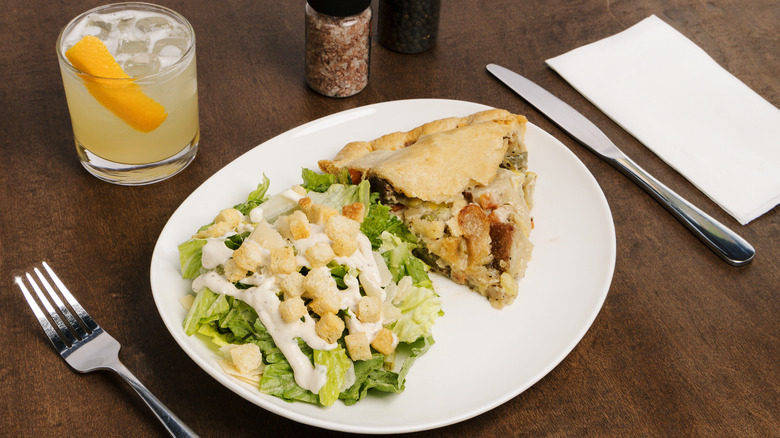 Pie, salad, and cocktail on wooden table with utensils, napkin, and seasoning