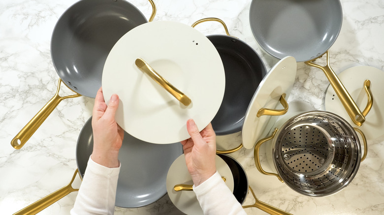 Hand holds white lid over pots and pans on marble countertop