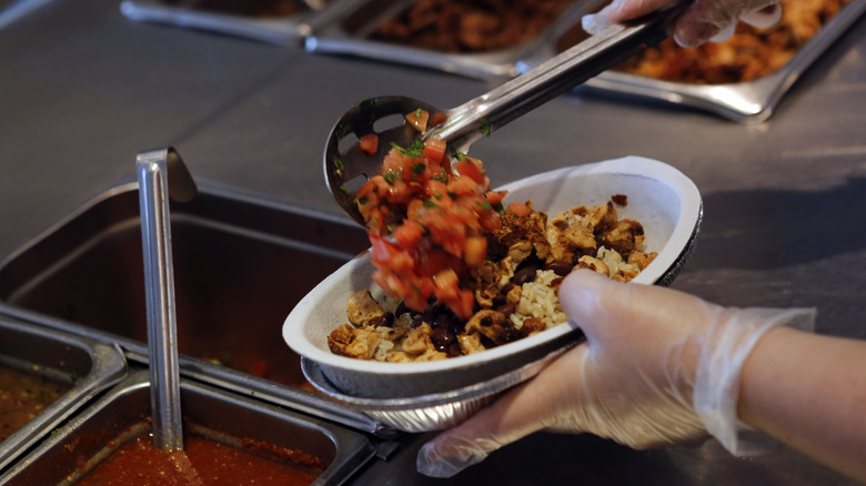 Chipotle employee filling burrito bowl