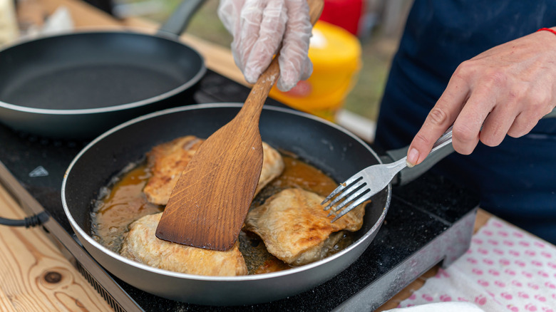 A chef cooking fish in a pan, using a spatula and a fork to move the fish around.