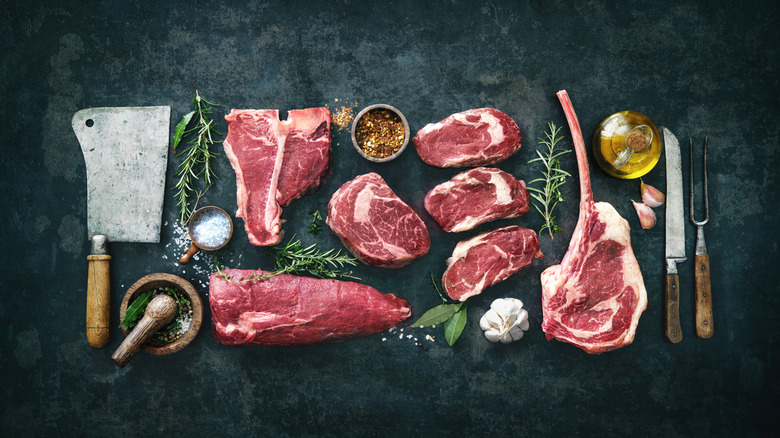 various raw cuts of beef roasts and steaks on dark background