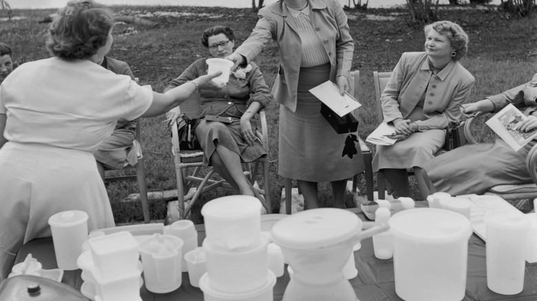 An outdoor party, with a host passing a piece of Tupperware to an attendee