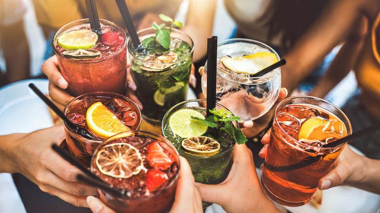 A group of people toasting with a colorful array of iced and garnished cocktails.