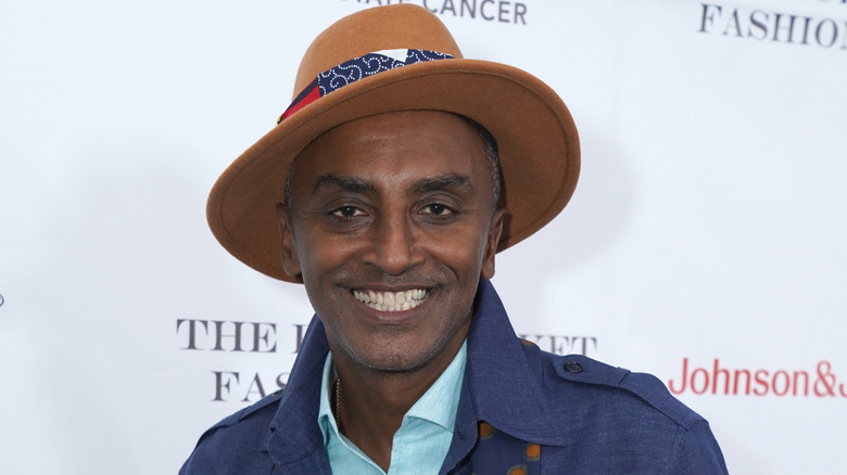 Marcus Samuelsson in an orange hat powder blue shirt and dark blue jacket smiling to camera.