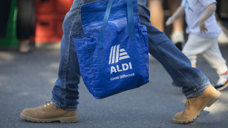 man holding Aldi shopping bag while crossing the street