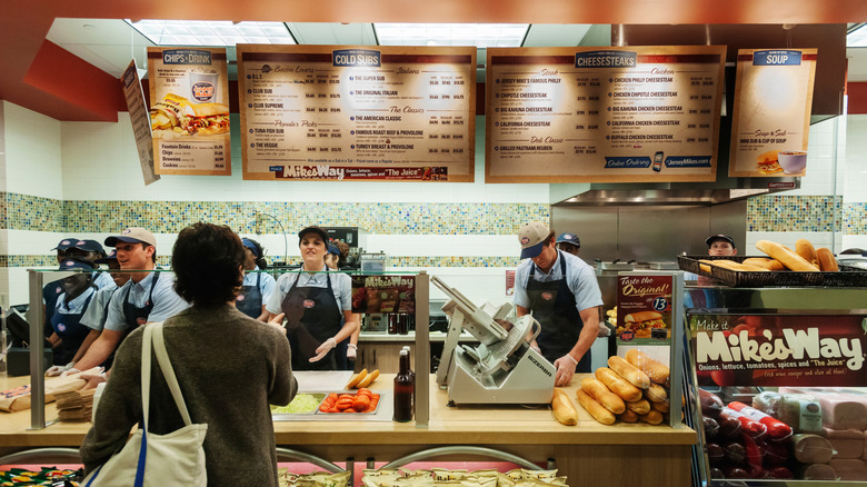 Customer standing at the counter at Jersey Mike's while employees make subs