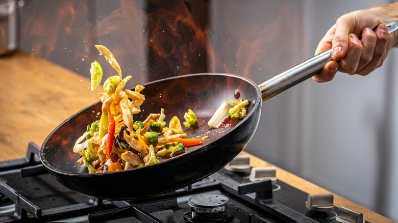 Person tosses food in pan