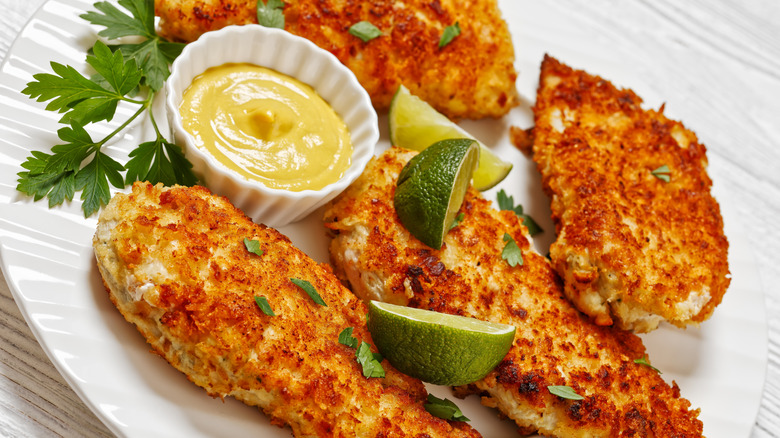 Parmesan-crusted chicken on a plate with lime, cilantro, and dipping sauce