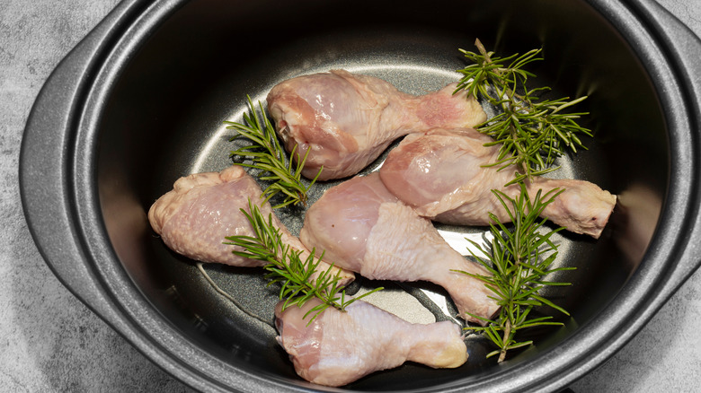 Raw chicken drumsticks in a slow cooker with parsley