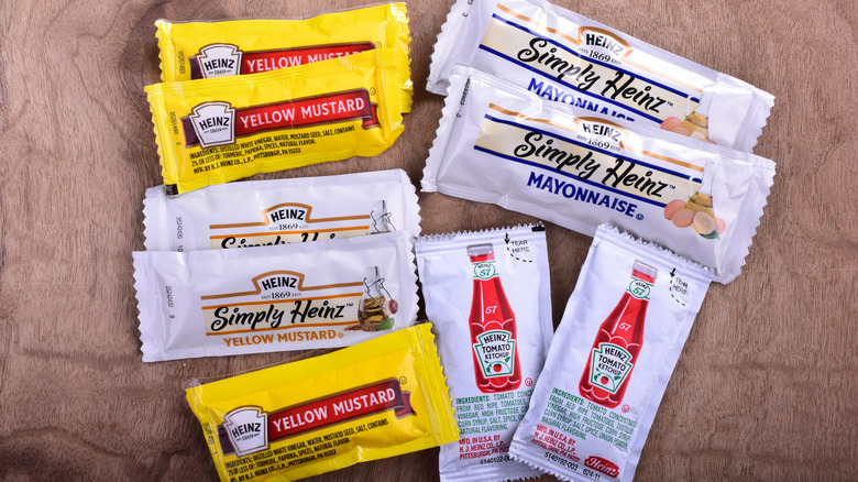 Mustard, ketchup, and mayo packets on wooden surface