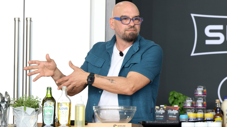 Michael Symon gesturing on stage kitchen with food