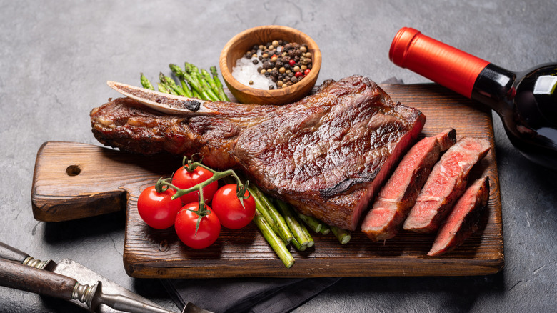 A nicely seared Tomahawk steak partially sliced open, with tomatoes and asparagus