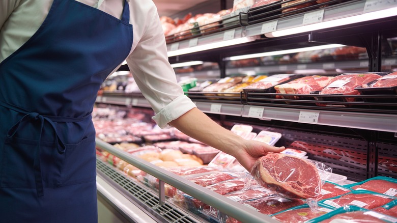 Employee placing packaged steak in refrigerated meat display at grocery store