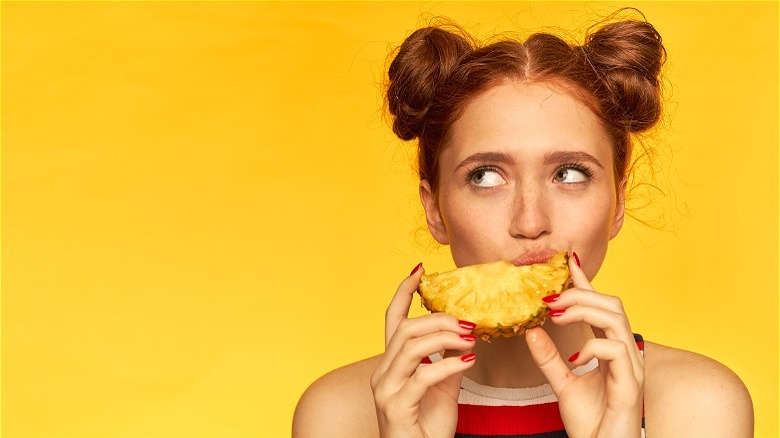 Person biting into pineapple slice