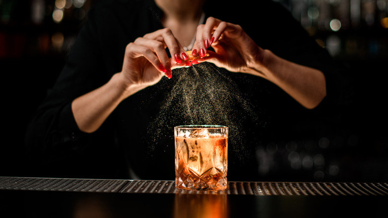 Bartender expressing an orange peel over an Old Fashioned cocktail.