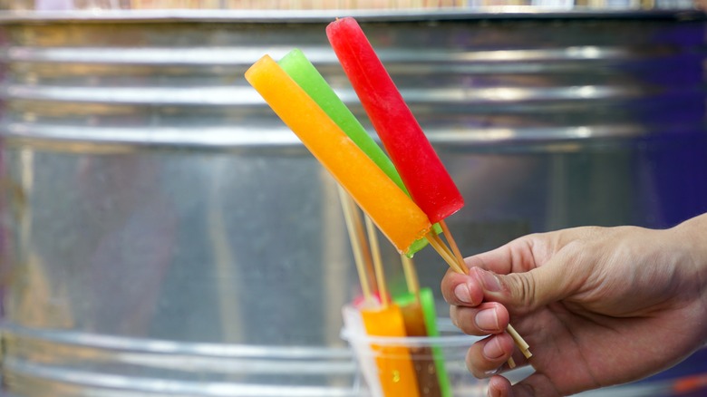 Person holding handmade popsicles in front of metal bin